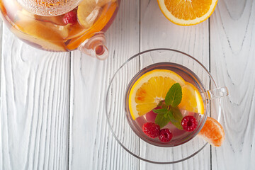 Fruit tea with berries, oranges and mint in a glass cup on a white background
