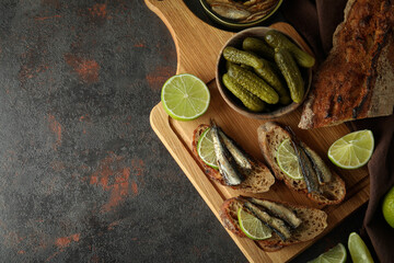 Board with sandwiches with sprats on textured background