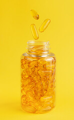 Fish oil capsules falling into the bottle on yellow background. Nutrition supplement and health care concept.