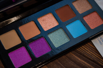 Black palette of colorful eye shadows on the wooden background.