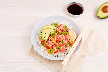 Poke bowl with salmon, rice, avocado, micro greens, pepper and soy sauce on white wooden background. Hawaiian diet food with fish. Top view. Flat lay. 