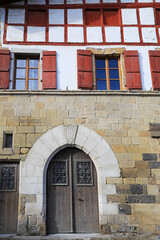 Fototapeta na wymiar fachada de casa con ventanas rojas y puerta medieval arco en espelette pueblo vasco francés francia 4M0A8119-as21