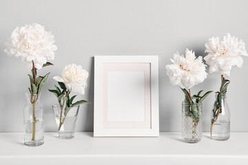Elegant white peonies flowers and white frame on table wall background. Mockup for text or artwork