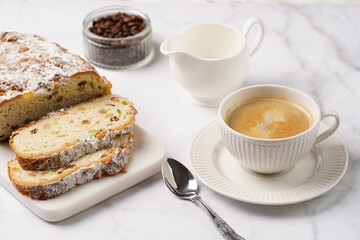 White porcelain cup with coffee cappuccino on a white saucer plate and christmas pastry stollen on a marble table