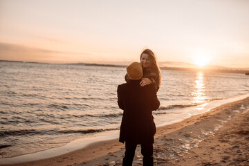 Young beautiful couple on a walk by the sea in autumn in the off-season, hugging, walking, smiling