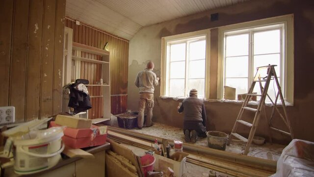 TRACKING CINEMATIC shot of 2 men plastering walls with clay, home improvement
