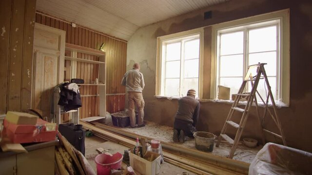 TRACKING shot R2L of 2 men plastering walls with clay, home improvement