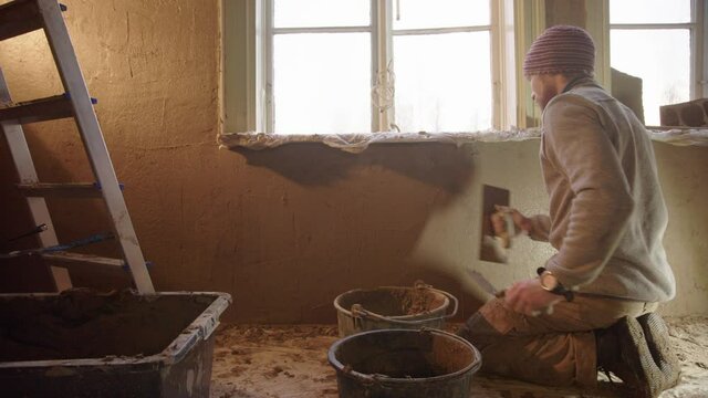 A professional plasterer smoothing the clay render on the walls under window