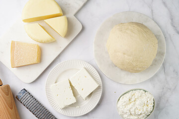 Various cheese types on marble and porcelain plates and fresh dough - ingredients for traditional georgian open pie khachapuri