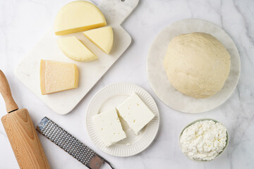Various cheese types on marble and porcelain plates and fresh dough - ingredients for traditional georgian open pie khachapuri