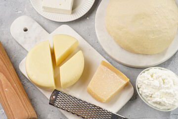 Various cheese types on marble and porcelain plates and fresh dough - ingredients for traditional georgian open pie khachapuri