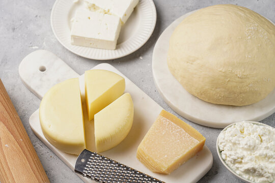 Various cheese types on marble and porcelain plates and fresh dough - ingredients for traditional georgian open pie khachapuri