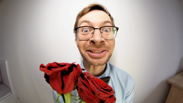 Fisheye portrait of young male nerd in glasses and elegant outfit with bow tie holding red rose and looking at camera. Valentine's day concept.