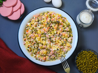 Russian holiday dish - olivier salad in a large bowl, ingredients and burgundy kitchen towel on blue background