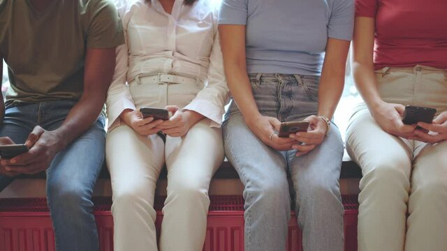 young people in casual clothes using mobile phones while sitting together on the window sill - no faces - slow motion