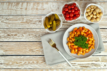 Beans with carrots in a white bowl. Beans with pickled tomatoes, mushrooms and cucumbers on a white background. Food on a shabby table. Bowl on an old wooden board.