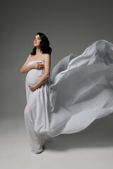 Caucasian young beautiful pregnant woman with dark hair in white fluttering fabric posing on a white background. isolates the banner space for text. Antique style