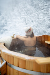 Woman relaxing in hot bath outdoors, sitting back and enjoying beautiful view on snowy mountains....