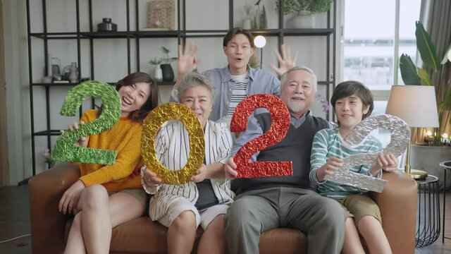 happiness asian multi generation 2022 new year celebrate,asian family hold 2022 text number on sofa at living room with laugh smile cheerful moment together,grandparent grandson parent sit relax sofa