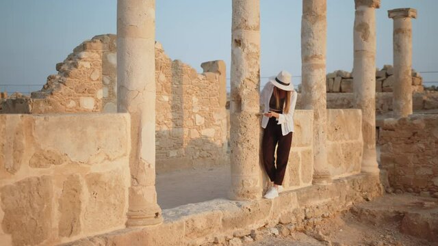 Competent female archeologist standing among ruins of ancient temple. Woman holding brush for digging and map in hands. Girl In an ancient temple with columns looking at records of a map.