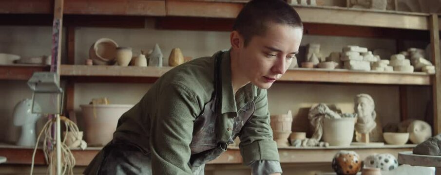 Tilt up shot of young Caucasian woman in apron using laptop in pottery workshop