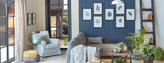 Modern grey sofa in the blue room with leaf frame, blanket , middle table, lamp, armchair, garden view.