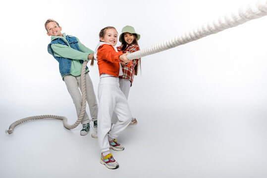 cheerful preteen children pulling rope while playing tug of war game on white.