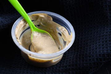 Peanut sauce in a plastic container with a spoon close-up. The sauce is in a disposable container. Portion container for sauce for salad.