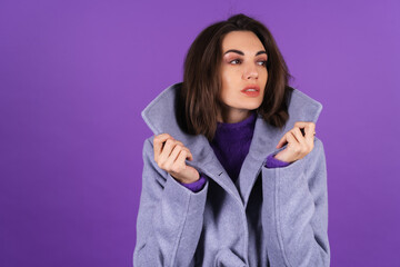 Fototapeta premium Young woman in a gray coat on a purple background posing, cozy and warm, autumn winter style