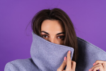 Fototapeta premium Young woman in a gray coat on a purple background posing, cozy and warm, autumn winter style