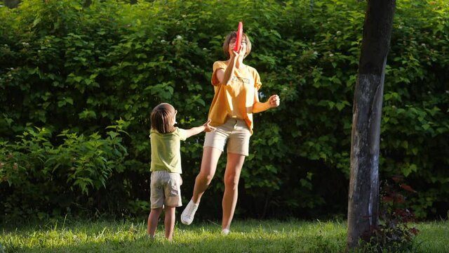 Mother and son play frisbee on grass lawn. Summer vibes. Outdoor leisure activity. Family life. Sports game at backyard.