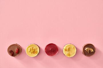 Colorful raw vegan mini cheesecakes on pastel pink background, top view