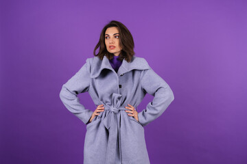 Young woman in a gray coat on a purple background posing, cozy and warm, autumn winter style
