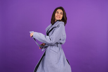 Young woman in a gray coat on a purple background posing, cozy and warm, in an autumn-winter style,...