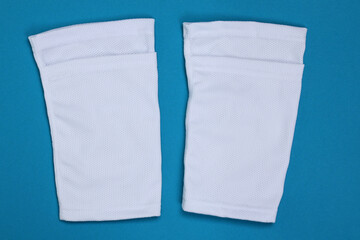 Football shin guards in white fabric. Shin sleeves made of polyester on a light blue background. White shield holders. Football ammunition for athletes.