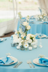 Wedding tables for guests. Round tables with a blue tablecloth. Decorated with flowers, plates, glasses and more