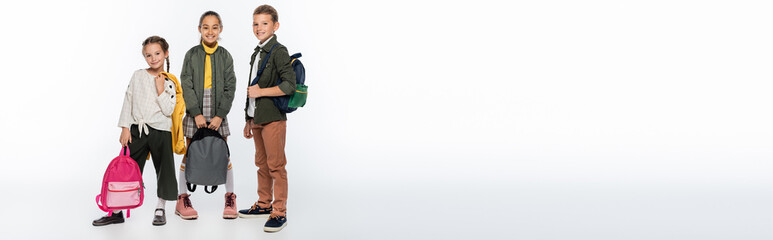 Obraz premium cheerful schoolboy and joyful schoolgirls standing with backpacks on white, banner.