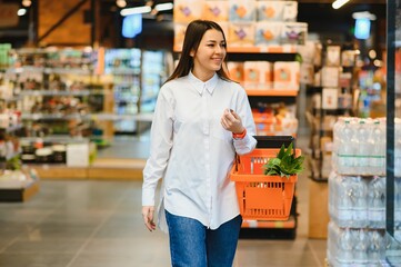 Shopping woman looking at the shelves in the supermarket. Portrait of a young girl in a market store with shopping cart at alcohol sector.