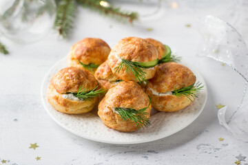 Cheese profiteroles with cream cheese, cucumber and herbs, gougeres, traditional French pastries, in white plate on a light gray background, top view. Delicious snack for New Year's table or buffet