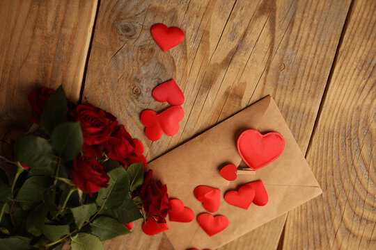 A bouquet of red roses and a letter with hearts on a wooden background. Picture for Valentine's Day. The concept of gifts and lovers. High-quality photography
