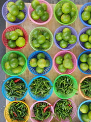 West Indian lemons (Citrus aurantifolia Swingle) and organic paprika (Capsicum annuum) are arranged in colorful plastic baskets for sale to customers who love spicy foods such as tom yam, papaya salad
