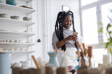 Female pottery artist using smartphone in her art studio 
