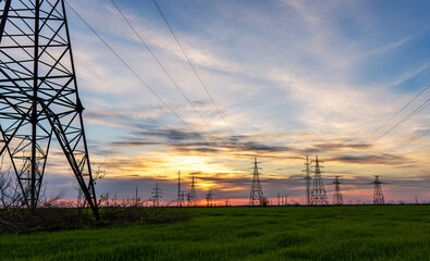high voltage power lines in the field against the backdrop of a bright and colorful sunset or dawn