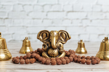 Bronze statue of Lord Ganesha, hindu God. Rudraksha rosary for meditation and set of metal bells for ceremonies on bright wooden background.