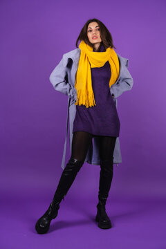 Young woman in a gray coat, knitted dress and in a yellow scarf on a purple background, full growth, spring winter style