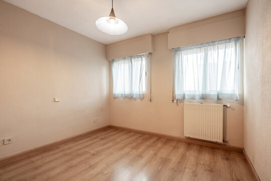 Empty room with salmon painted walls and oak joinery and windows with plain curtains and aluminum radiator.