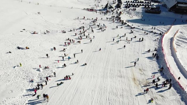 A lot of people having fun on mountain. Group of tourists walking, skiing and sledding slope in winter. Aerial drone view of children on the snow. Winter holidays.
