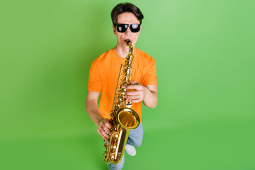 Photo of cool charming young man hold hands play sax wear sunglass hobby isolated on green color...