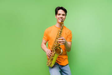 Photo of cheerful happy young joyful man hold hands saxophone smile music isolated on green color...