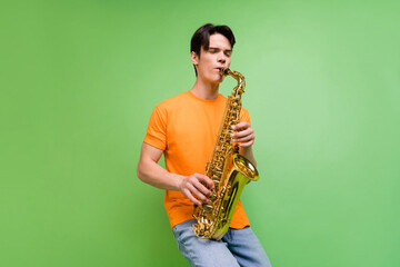 Photo of cheerful young happy man enjoy play saxophone musician artist isolated on green color...